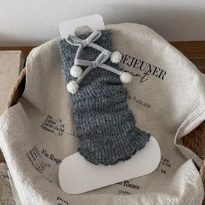 Grey knitted leg warmers with velvet bows and pom-poms, cozy winter fuzzy slouch socks.