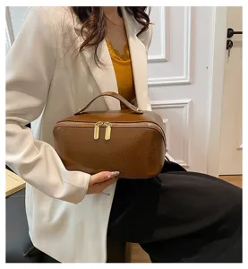 Detail view of a solid brown PU leather cosmetic bag with double zippers and top handle.
