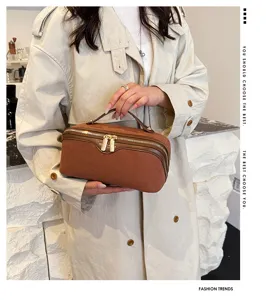 Brown suede cosmetic bag detail showing soft texture, dual zippers, and elegant top handle.