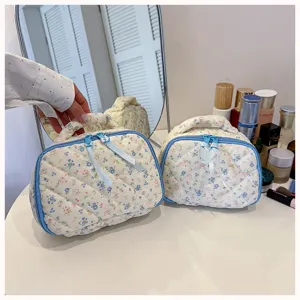 Quilted floral cosmetic bag with blue zipper and portable handle, elegant makeup storage pouch.