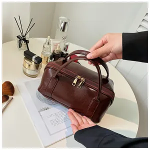 Brown leather cosmetic bag with double zippers and portable handles for daily travel storage.