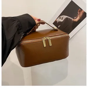 Brown PU leather cosmetic bag with top handle and double zippers for daily travel use.