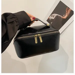 Black PU leather cosmetic bag with dual zippers and top handle for travel and daily storage.