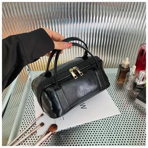 Detailed view of black patent leather cosmetic bag with dual handles and gold zippers.