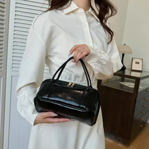 Black glossy leather cosmetic handbag held by model, stylish travel makeup storage pouch.