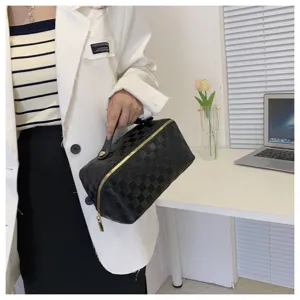 Detail shot of black checkerboard cosmetic bag with gold zipper and portable handle.