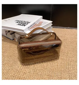 Vista dettagliata della borsa cosmetica trasparente con manico marrone e zip per organizzare tutto.