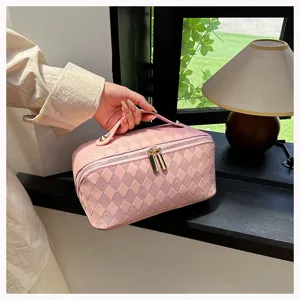 Detail shot of pink quilted PU leather makeup bag with handle and dual zippers in indoor setting.
