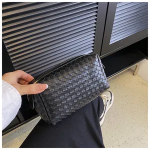Black woven leather cosmetic bag, detailed hand holding view, luxury style travel pouch.