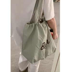 Detail view of casual nylon drawstring shoulder tote bag in sage green with brown lettering.