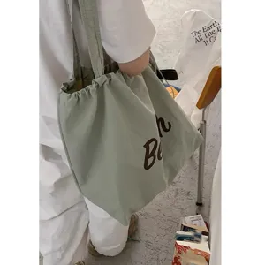 Detail shot of a light green nylon drawstring shoulder bag with brown letter print casual use.