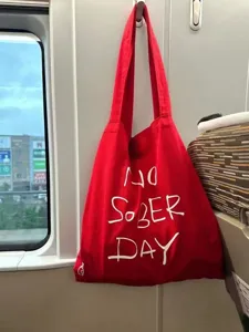 Red canvas tote bag detail view, casual shoulder bag with handwritten letter print.