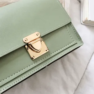 Detalle de primer plano de bolso bandolera cuadrado verde claro con cierre dorado.
