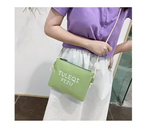 Canvas crossbody bag detail showcasing light green fabric and white letter print strap.