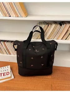 Black travel duffel bag detail showcasing bow embroidery, durable handles and spacious compartment.