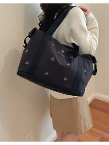 Detail shot of black travel duffel bag with bow prints and logo worn by model indoors.