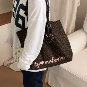 Detail view of the leopard print tote bag with heart stud charm and embroidered letter design.