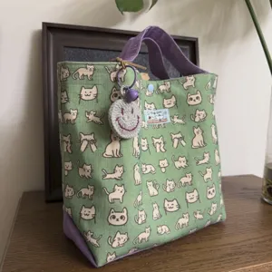 Detail view of mint green cat print canvas tote bag with purple handles and cute smiley charm.