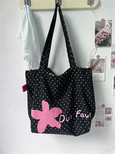 Close-up detail of black polka dot canvas tote bag with pink flower embroidery and cute text.