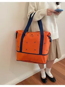 Detail shot of orange canvas travel tote bag with blue straps and bow embroidery for women.