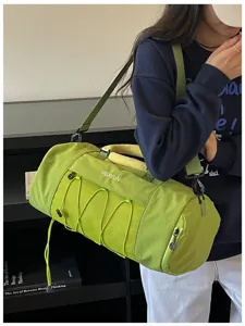 Green cylindrical gym duffel bag with mesh pocket and shoulder strap for travel and fitness.
