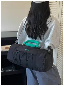 Detail view of large capacity black cylindrical sports duffel bag with green handle for gym.