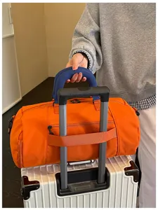 Travel duffel bag detail showing convenient luggage trolley strap and bright orange fabric design.