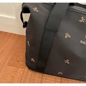 Black travel duffel bag detail, gold bow embroidery design, durable nylon fabric, spacious gym bag.
