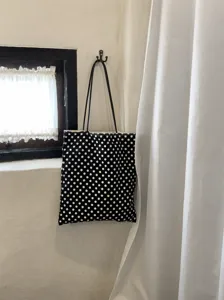 Detailed view of classic black and white polka dot canvas tote bag hanging on vintage room wall.