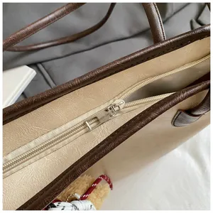 Close-up detail of women tote bag showing zipper closure, brown trim and leather texture.