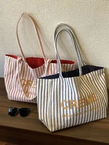 Detail view of French striped canvas tote bag with letter print and shoulder straps in daily scene.