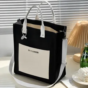 Closeup of black canvas tote bag front pocket and handle strap, showing durable fabric details.