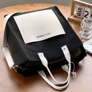 Detailed close-up view of the black canvas tote bag featuring contrast white pocket and strap.