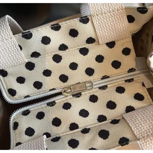 Detail view of a stylish canvas tote bag with classic black polka dots and secure zipper closure.
