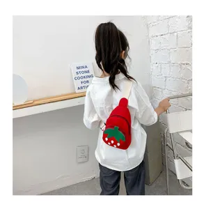 Detail view of the cute red strawberry canvas chest bag worn by a child model indoors.