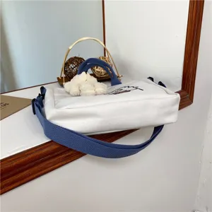 White canvas crossbody bag detail showing blue strap, sturdy handle and cute embroidery design.