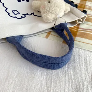 Close-up view of white canvas tote bag detail, featuring blue handles and cute plush bear.