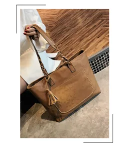 Close-up of brown PU leather tote bag featuring braided handles, tassel, and front pocket.