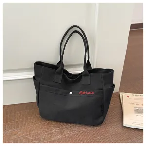 Close-up detail of the black canvas tote bag showcasing front pocket and zipper closure.