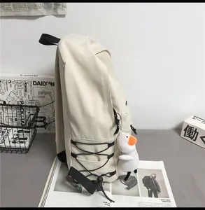 Minimalist beige backpack detail featuring side bungee cords and a cute duck plush pendant.