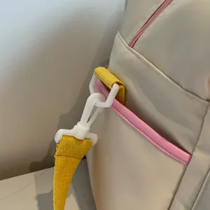 Taschenriemendetail mit strapazierfähigem gelben Gurtband, weißem Kunststoffhaken und rosa Akzent.