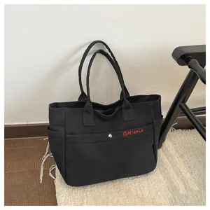 Details of black canvas tote bag with large capacity, dual handles and red embroidery front pocket.