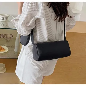 Detailed back view of a minimalist black cylindrical crossbody pillow bag styled casually.