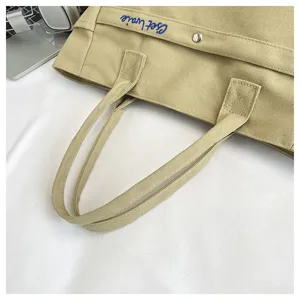 Canvas tote bag detail view, casual beige shoulder handbag with blue embroidery design.