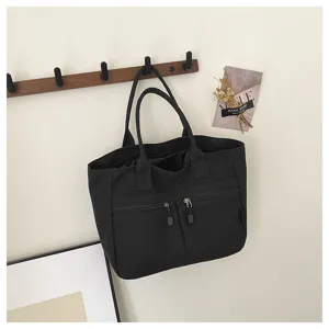 Black canvas tote bag with double handles and front zipper pockets, detailed view.