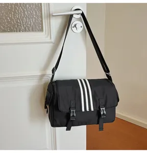 Black nylon messenger bag with sporty three-stripe design, detail view showing strap.