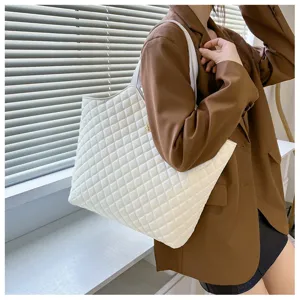 Close-up detail view of white quilted tote bag highlighting diamond texture and shoulder strap design.