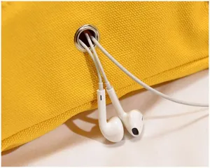 Yellow canvas bag detail shot showing headphone cable grommet hole with white wired earphones inside.