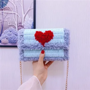 Gros plan du sac bandoulière en tricot pelucheux avec motif de cœur rouge et chaîne dorée.