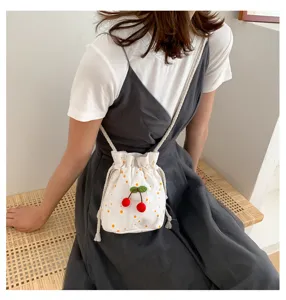 Vue détaillée du sac seau en toile blanche avec broderie de cerises mignonne et bandoulière.